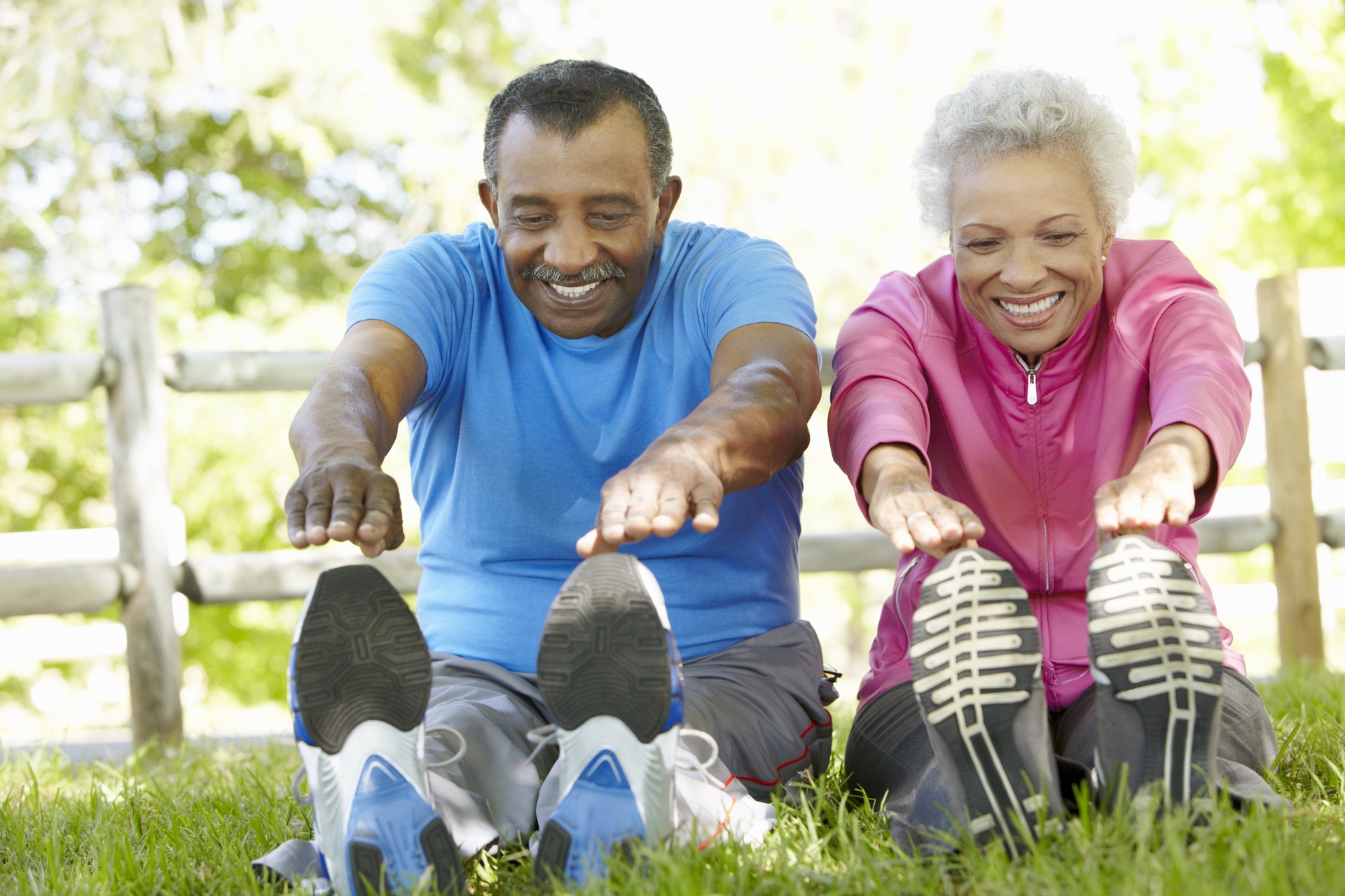 Senior African American Couple Exercising In Park Stretching To Touch Toes